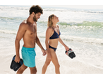 Cuplu pe plajă, femeie în bikini CRIVIT, bărbat ținând șlapi CRIVIT.