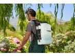 Man in overalls using a garden sprayer on pink flowers, with green foliage around.