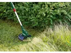 PARKSIDE® 20V Cordless Grass Trimmer cutting tall grass next to a hedge.