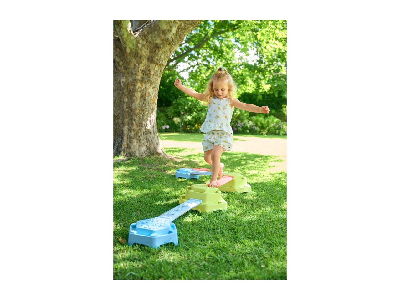 A young girl balancing on a colorful outdoor stepping stone set in a garden.
