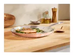 Salmon with potatoes and spinach in a copper frying pan on a wooden counter.