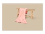 Pink blanket with red stitching draped over a wooden bench on a beige background.