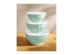 Stack of three mint green mixing bowls with white lids on a wooden surface.