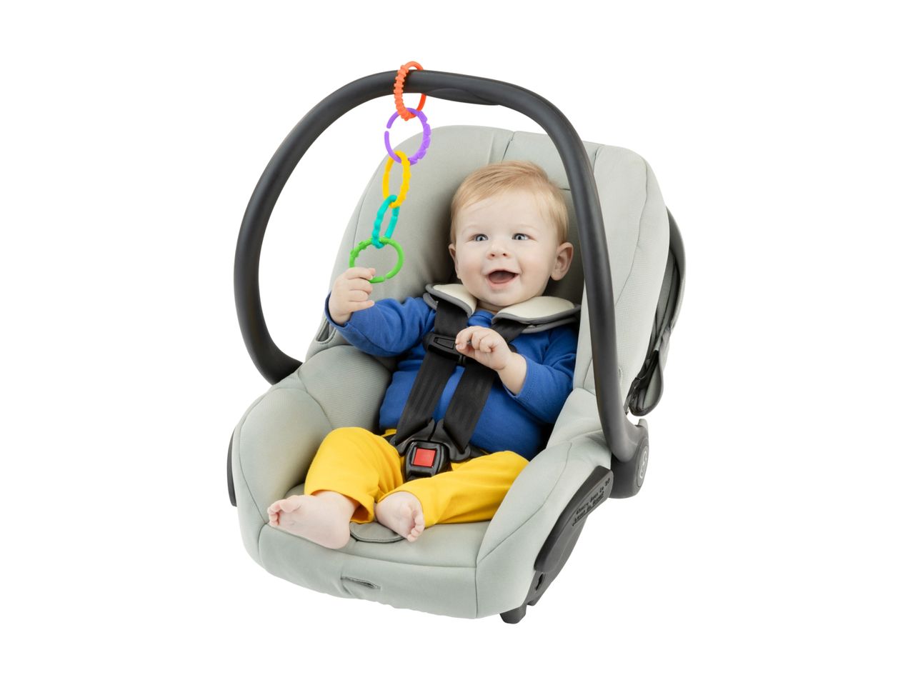 A happy baby in a car seat, playing with colorful rings.
