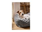 A small dog resting in a soft, grey textured pet bed on a wooden floor.