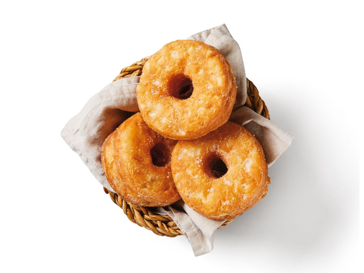 Három cukrozott fánk egy fonott kosárban, vászonkendőn.