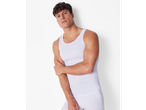 A man in a white ribbed tank top and white briefs, posing against a white wall.