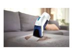 Cordless spot cleaner removing a stain from a grey sofa in a living room.