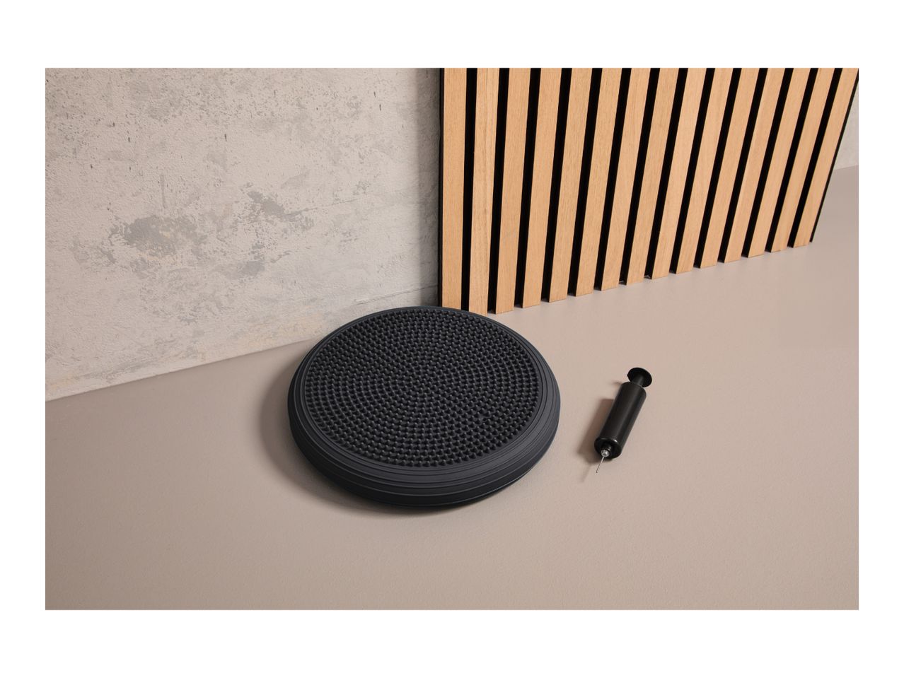 A black balance cushion with a pump on a light brown floor next to a concrete wall and wooden panels.