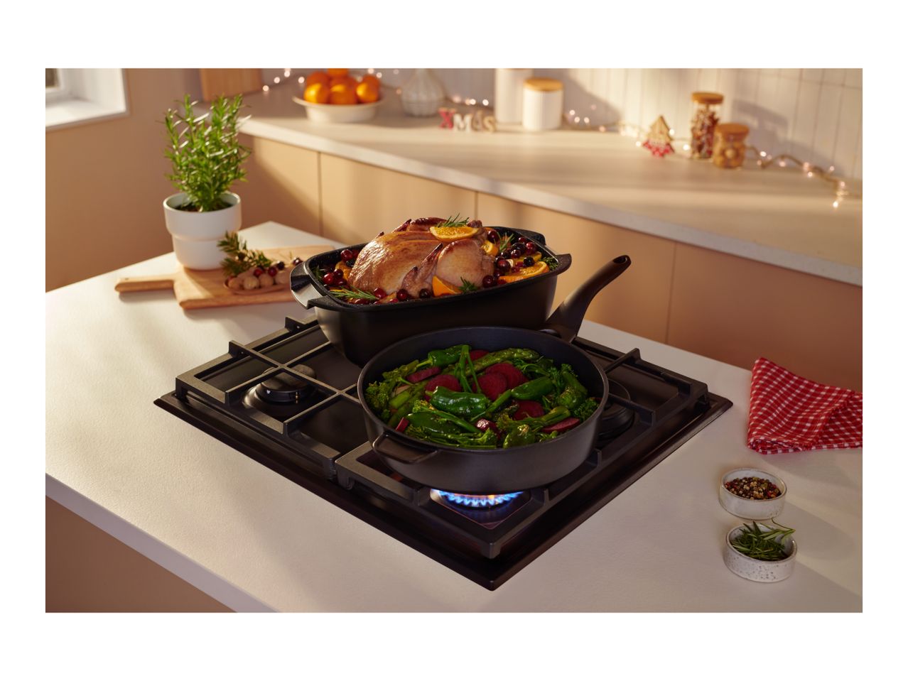 A roasted chicken and vegetables cooking in pans on a gas stove in a festive kitchen.