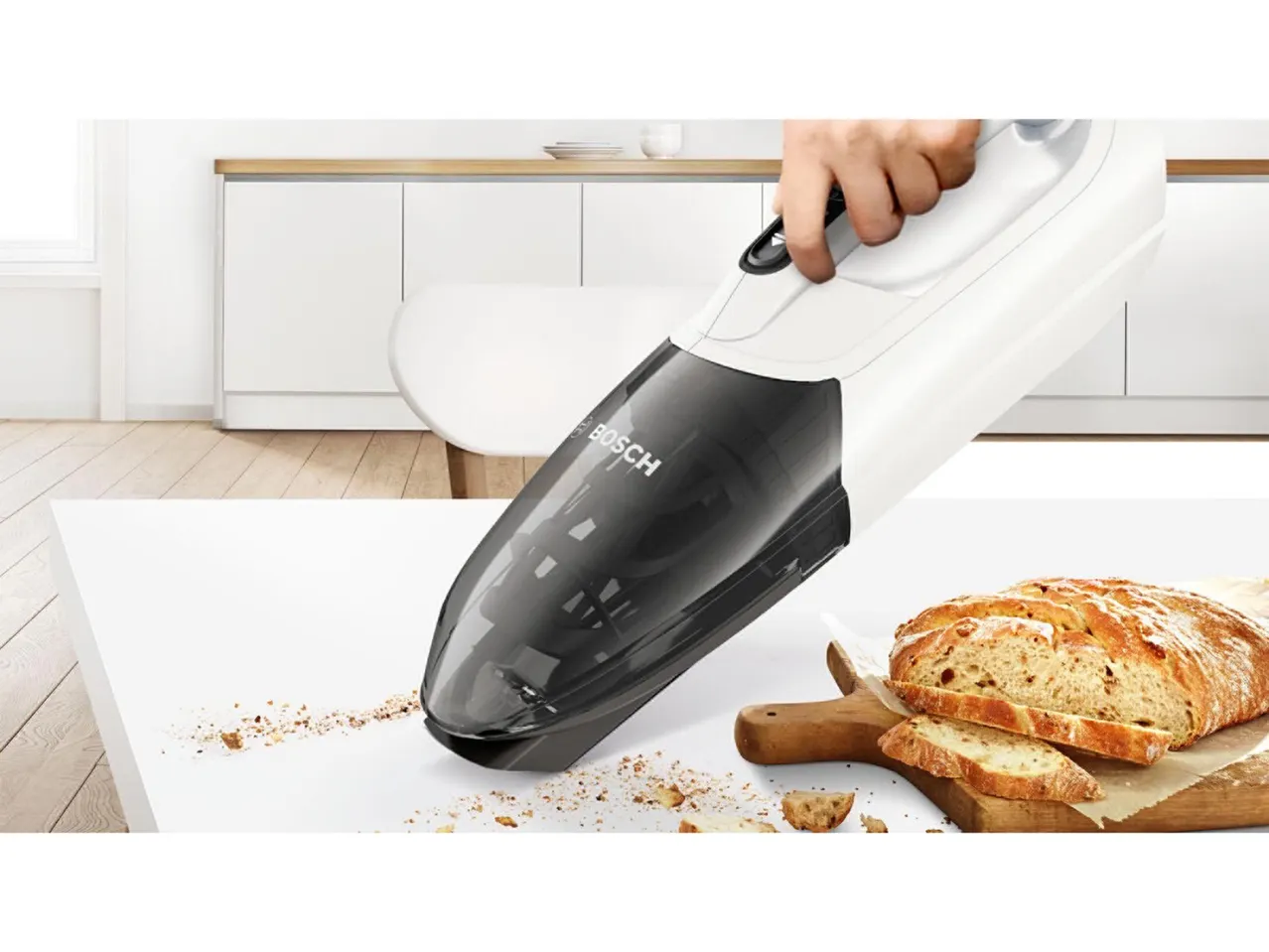 Bosch kézi porszívó morzsákat szív fel egy konyhaasztalról, frissen szeletelt kenyér mellett.