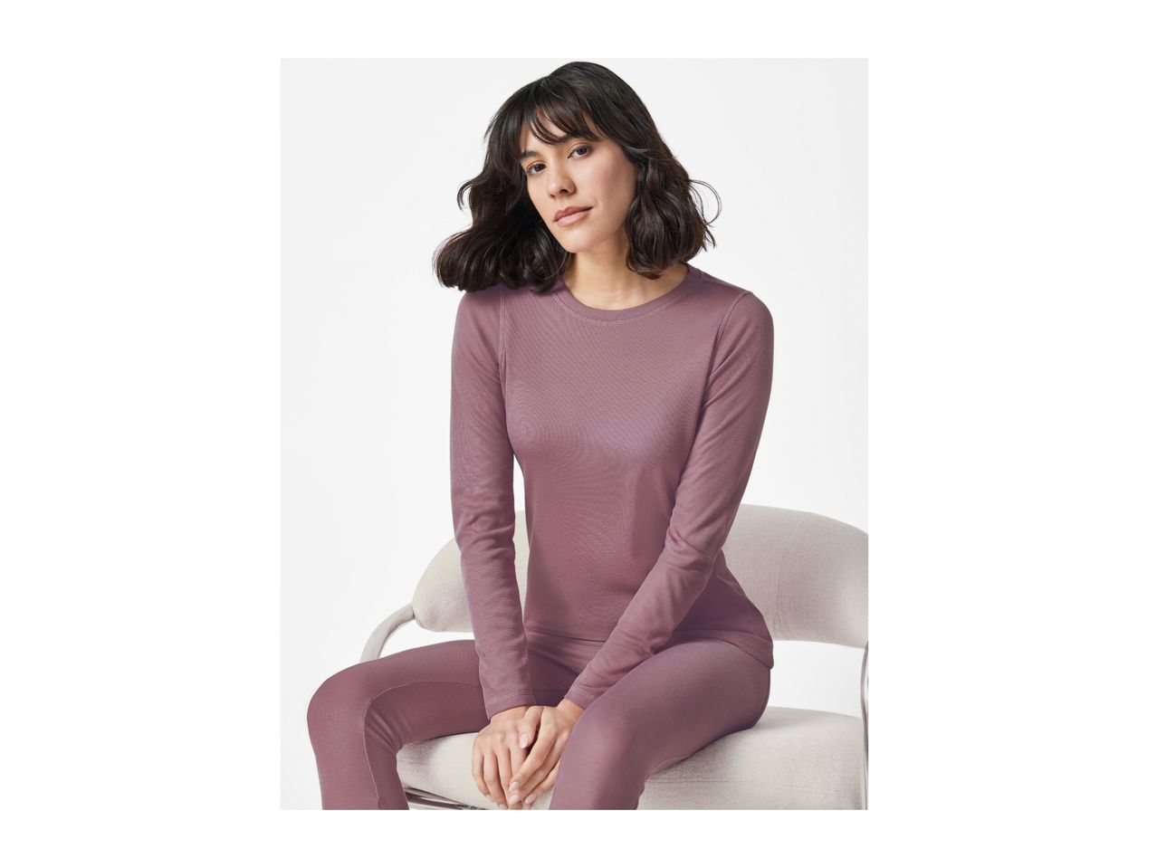 A woman in a long-sleeved mauve top and matching leggings sits on a chair.