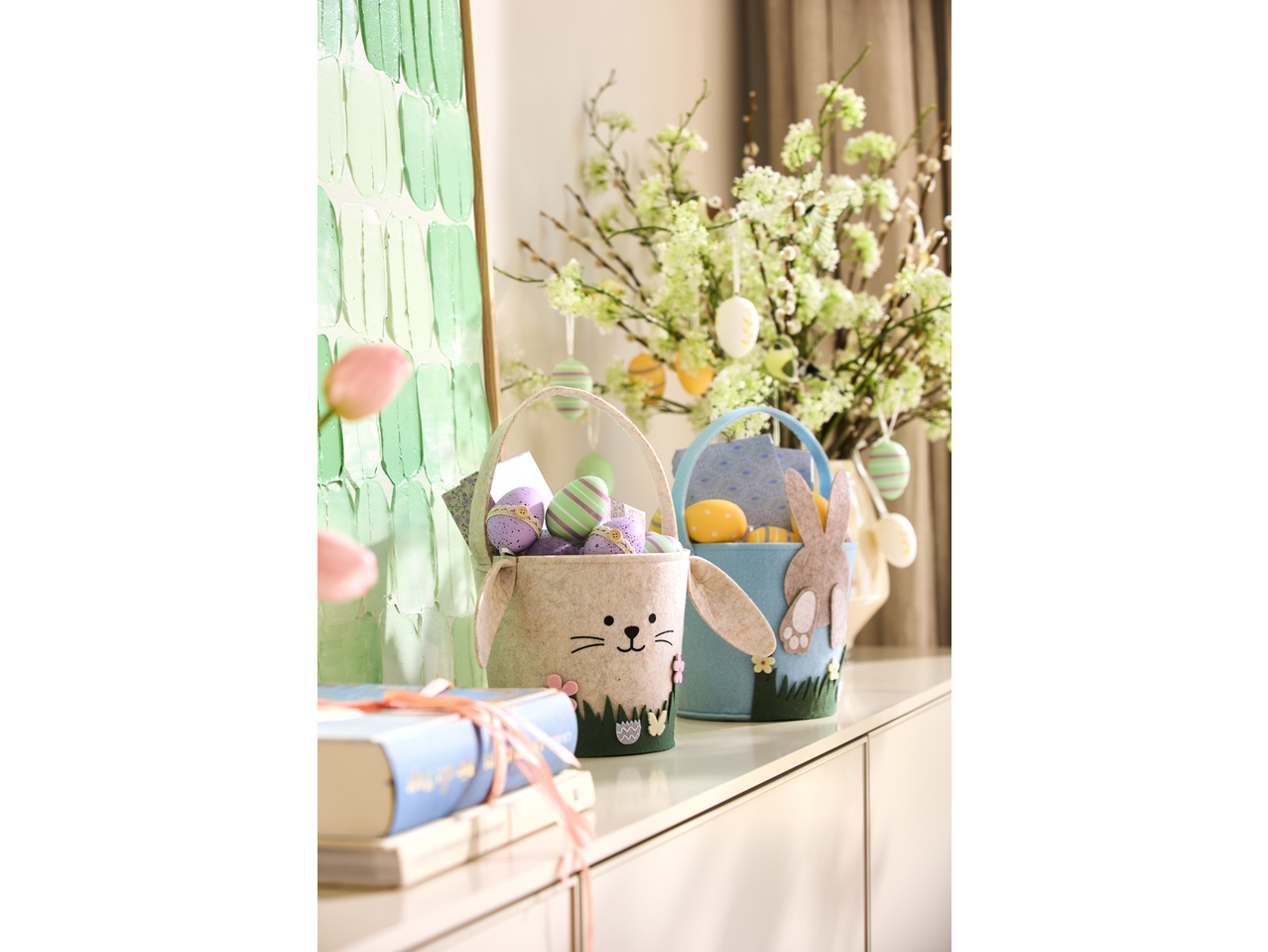 Zwei Filz-Hasenkörbe mit Ostereiern, neben einer Vase mit Zweigen.
