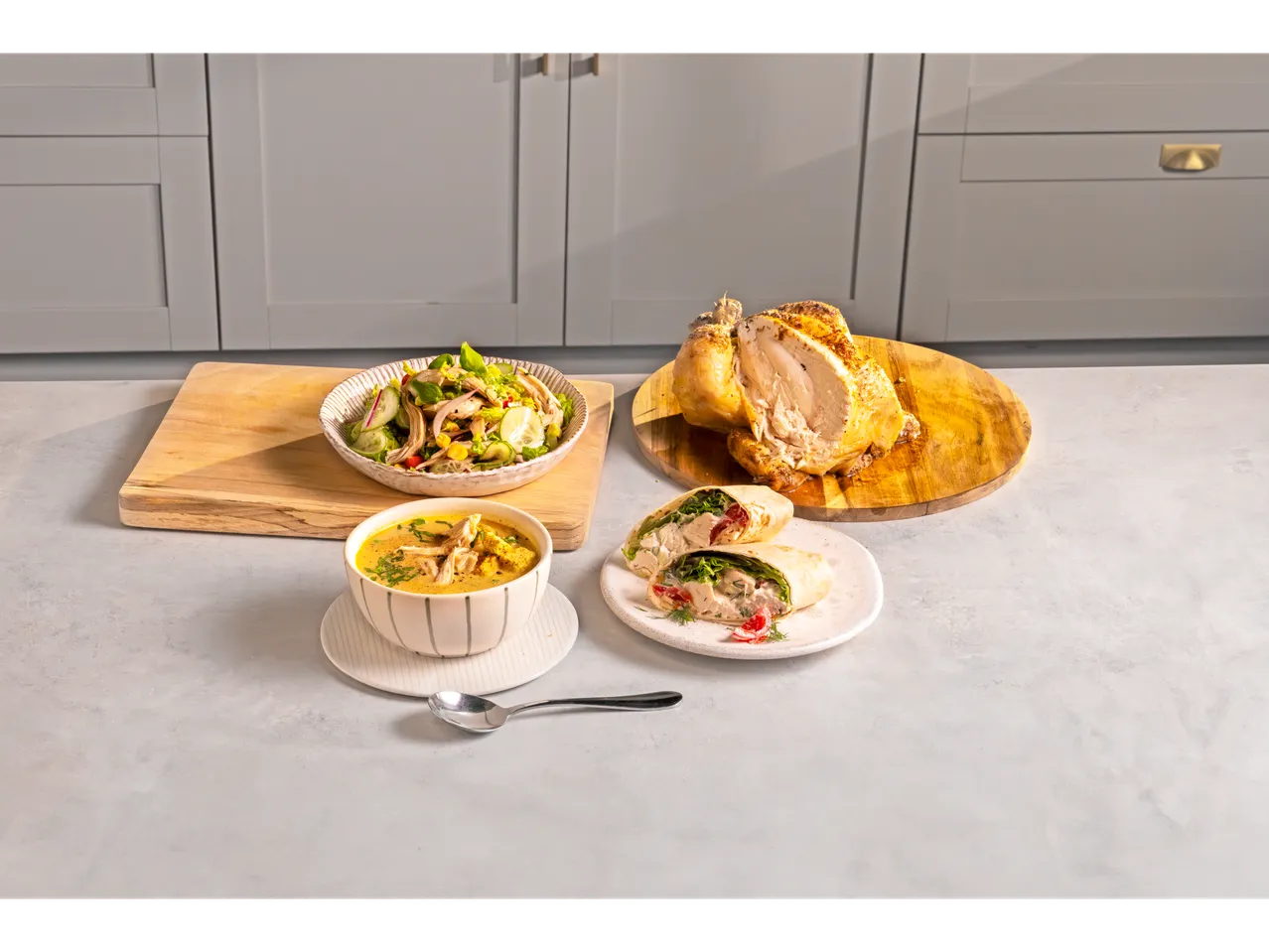 A roasted chicken is presented alongside a chicken salad, soup, and wrap.