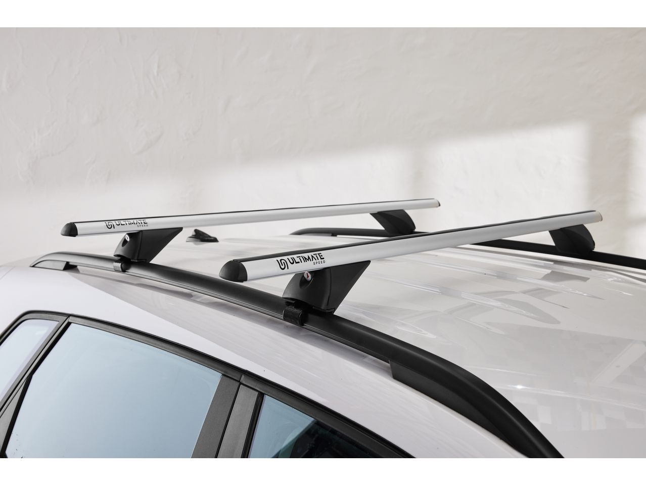 Silver car roof bars on a white car, with a white textured background.