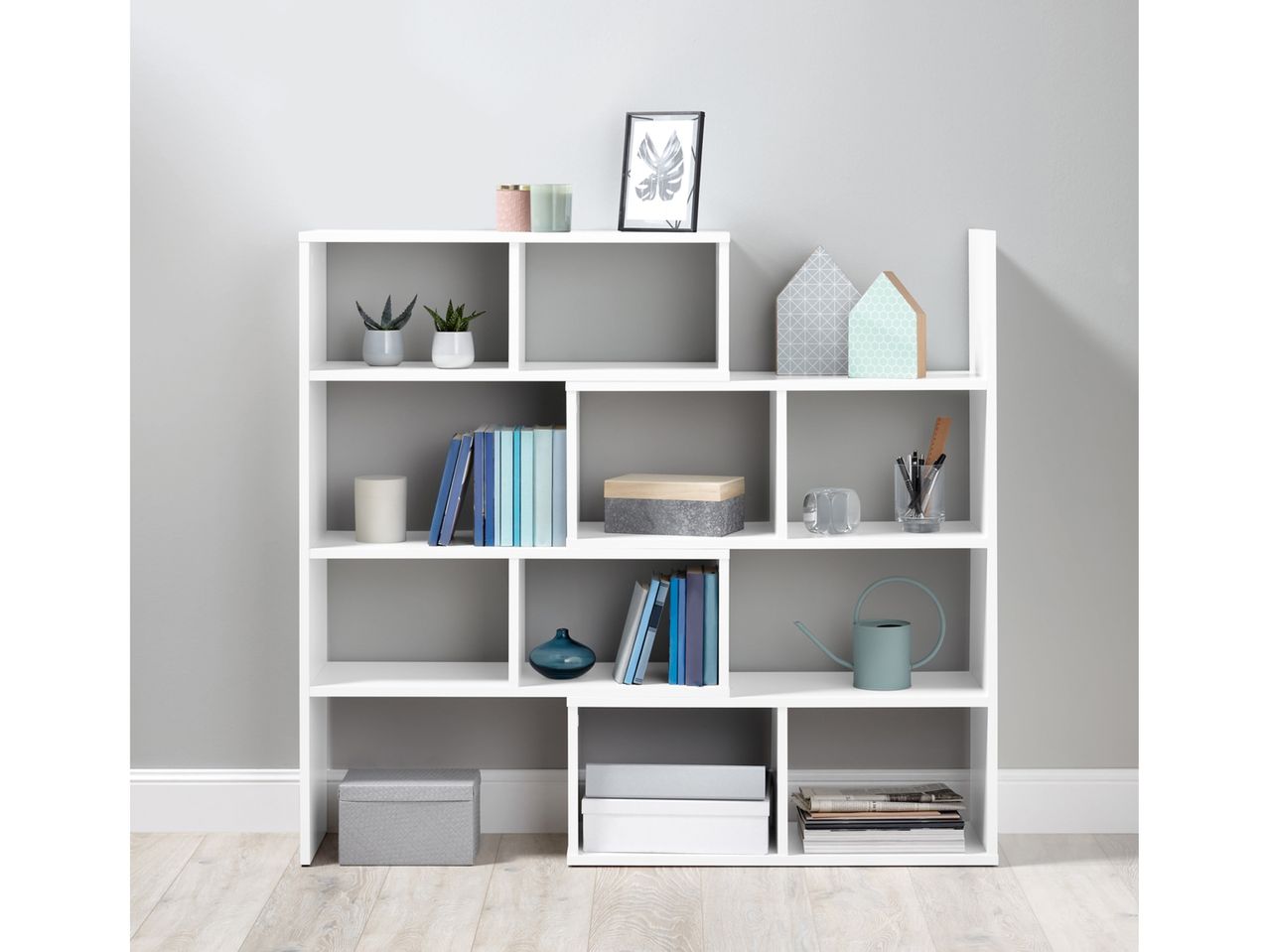 A white modular shelving unit filled with books, plants, decorative items, and storage boxes.