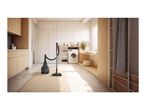 A black canister vacuum cleaner standing on a rug in a modern, bright laundry room.