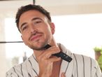 Man in a bathrobe trimming his beard with a beard trimmer.