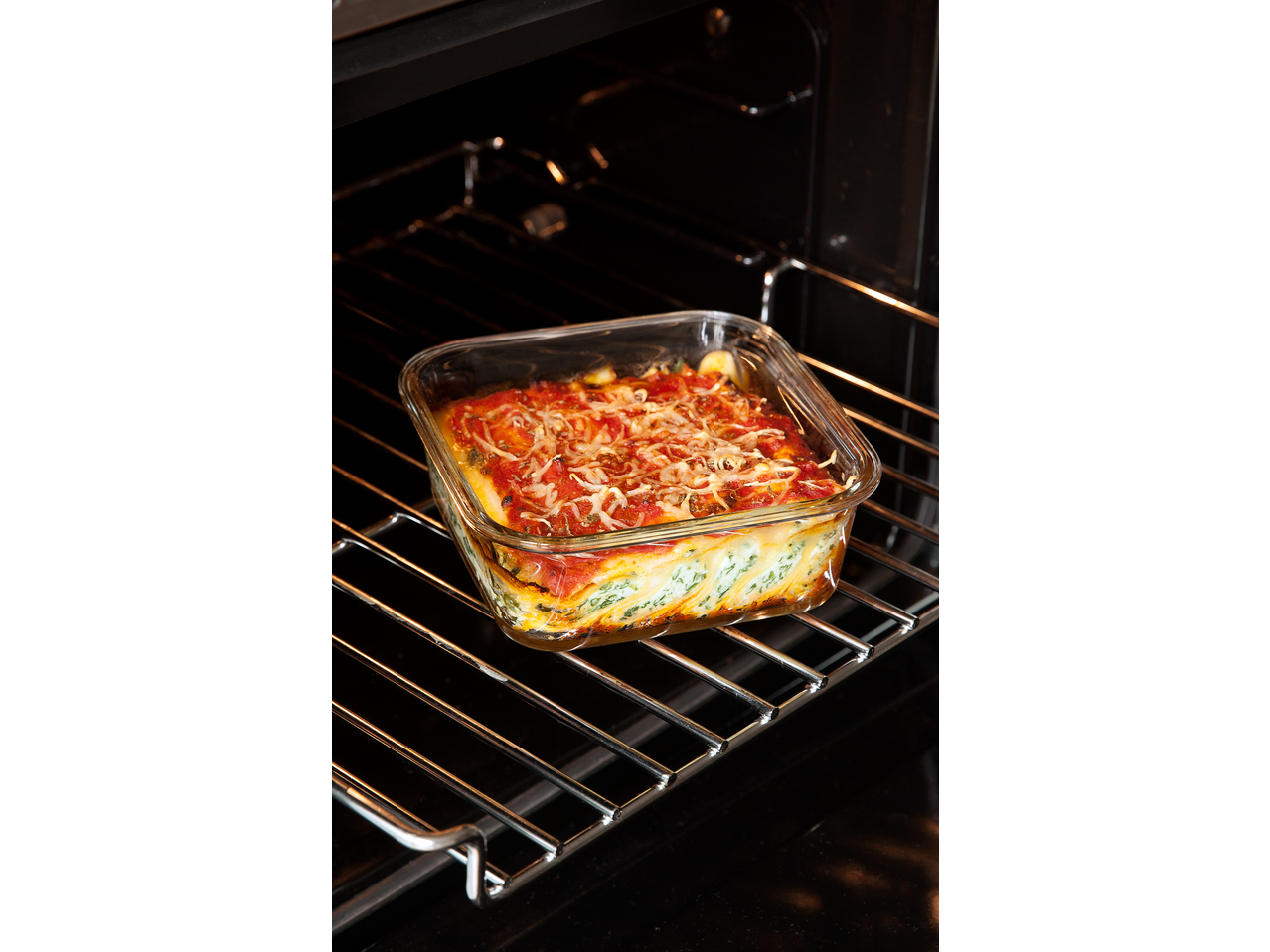 Vas de copt cu lasagna cu sos de roșii și brânză în cuptor.