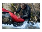 Man repairing a red kayak with a transparent patch by a river.