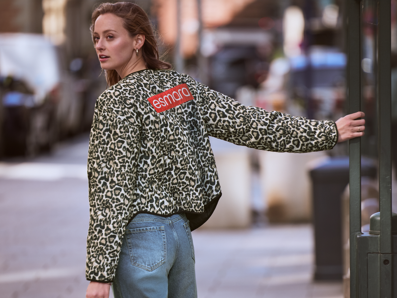 Жена в яке с леопардов принт Esmara и дънки, обърната назад на улицата.