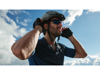 Man in cycling helmet, sunglasses, and gloves, looking up at a blue sky with clouds.