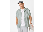 Man in a striped short-sleeve shirt, white t-shirt, grey shorts, and a grey cap.