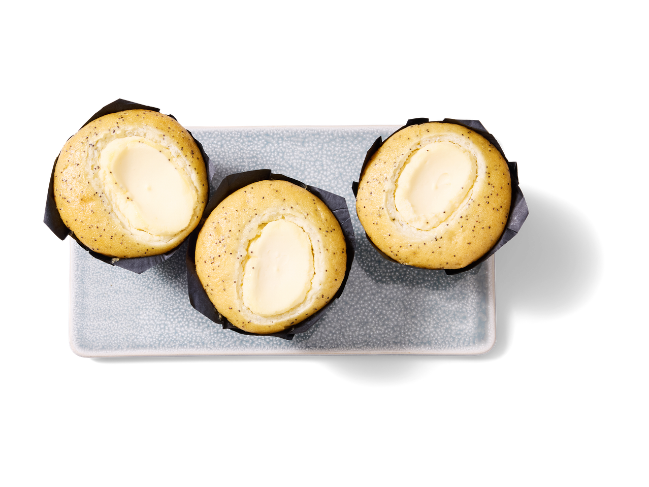 Drie muffins met roomkaasvulling en maanzaad op een lichtblauwe schaal.