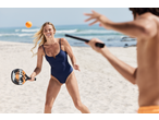 Femeie în costum de baie CRIVIT jucând tenis de plajă pe nisip.