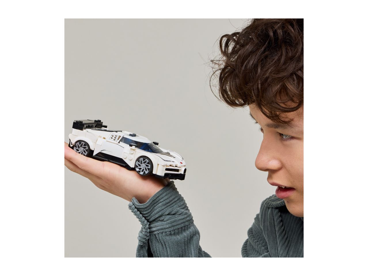 A person holding a white toy race car, looking at it intently.