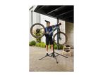 Man repairing a bicycle on a repair stand with tools on a wooden stool.