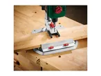 A Holzmann drill press is mounted on a workbench, drilling into a piece of wood.