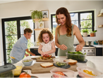 A family prepares healthy lunches together in a bright kitchen, using clear plastic food containers.