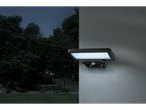 Lampă solară cu LED montată pe perete, iluminând o zonă exterioară întunecată.