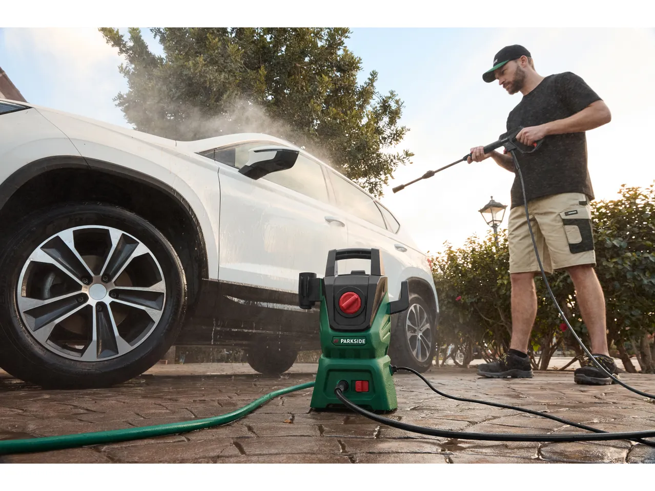 A man uses a Parkside pressure washer to clean his white SUV.