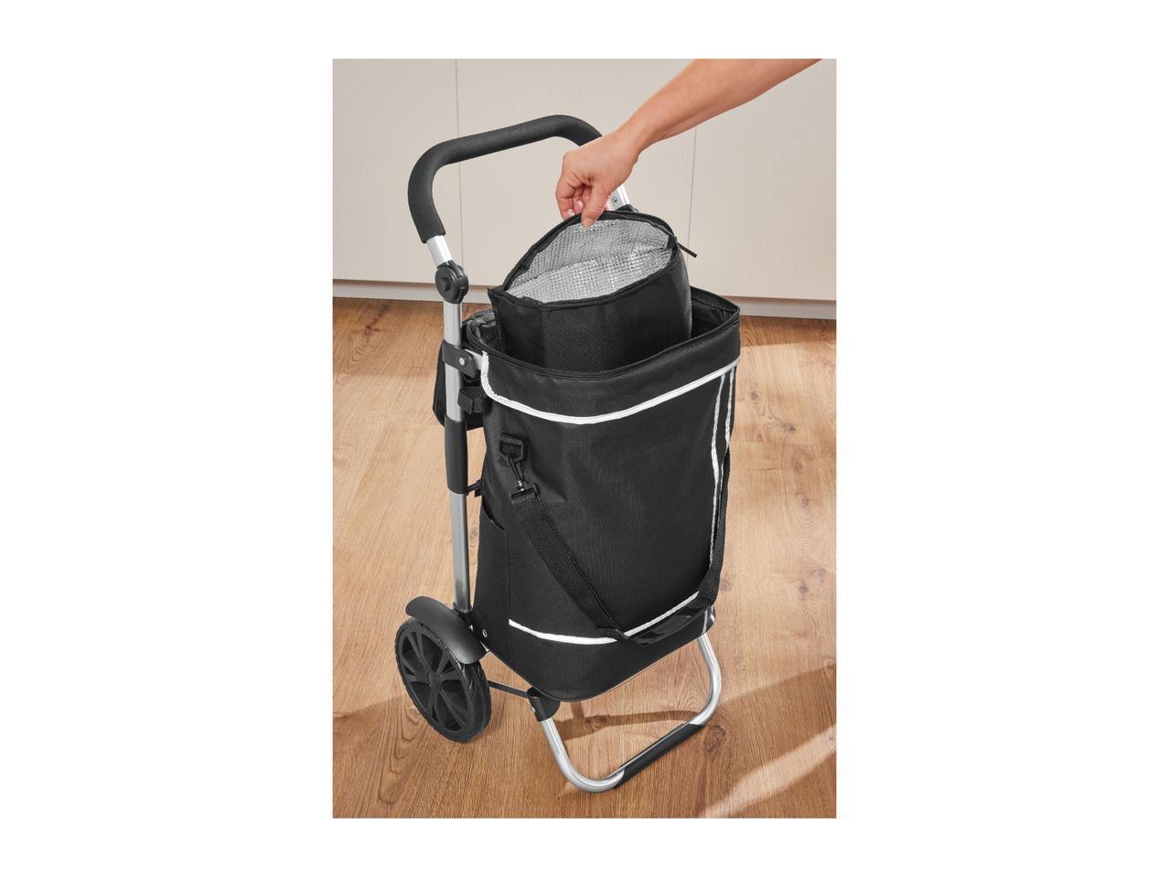 A person opening the insulated compartment of a black shopping trolley with wheels.