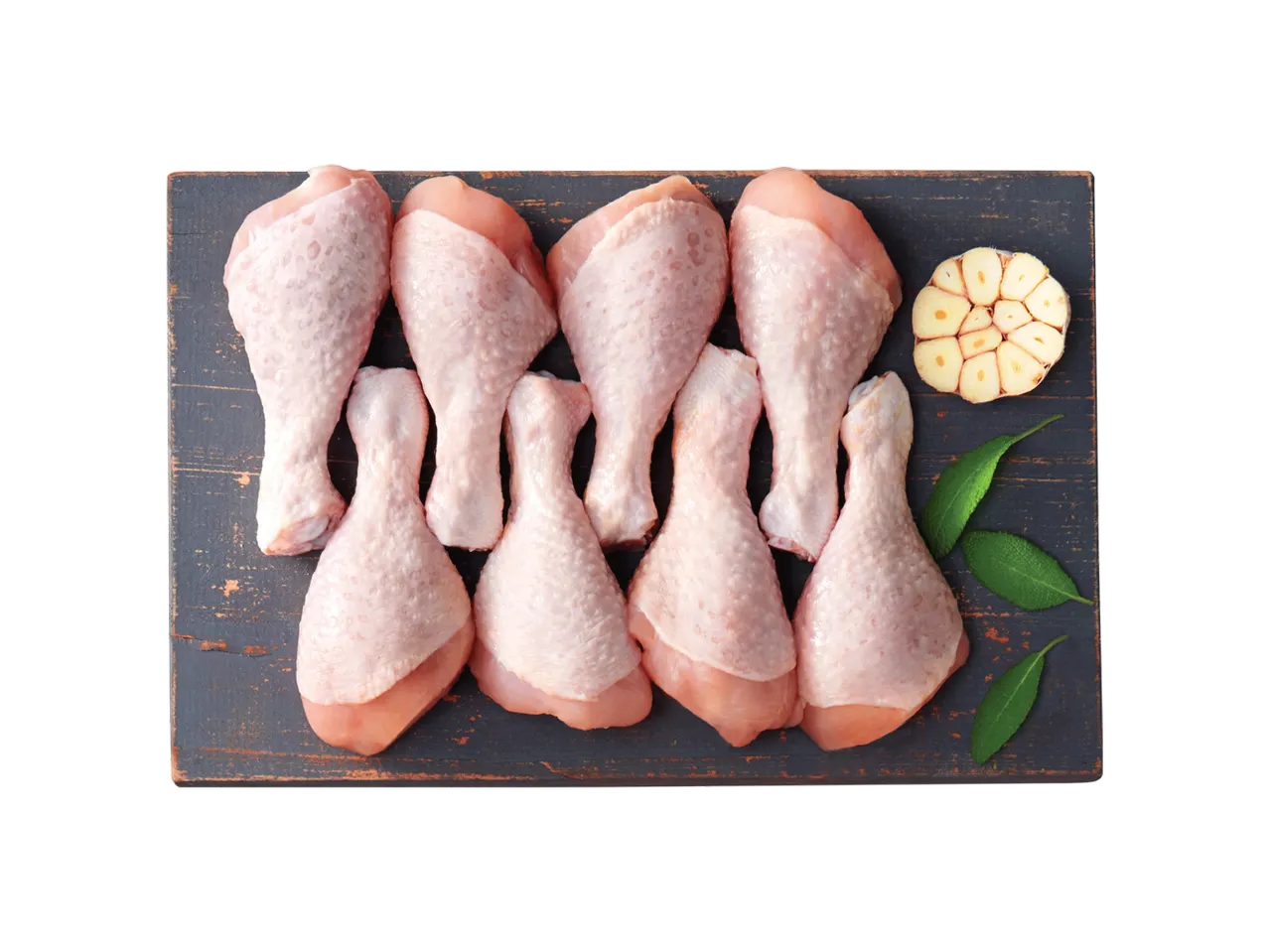 Šviežios vištienos blauzdelės su česnaku ir žolelėmis ant tamsios pjaustymo lentos.