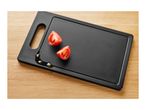 Black cutting board with two tomato halves and olive oil on a wooden surface.