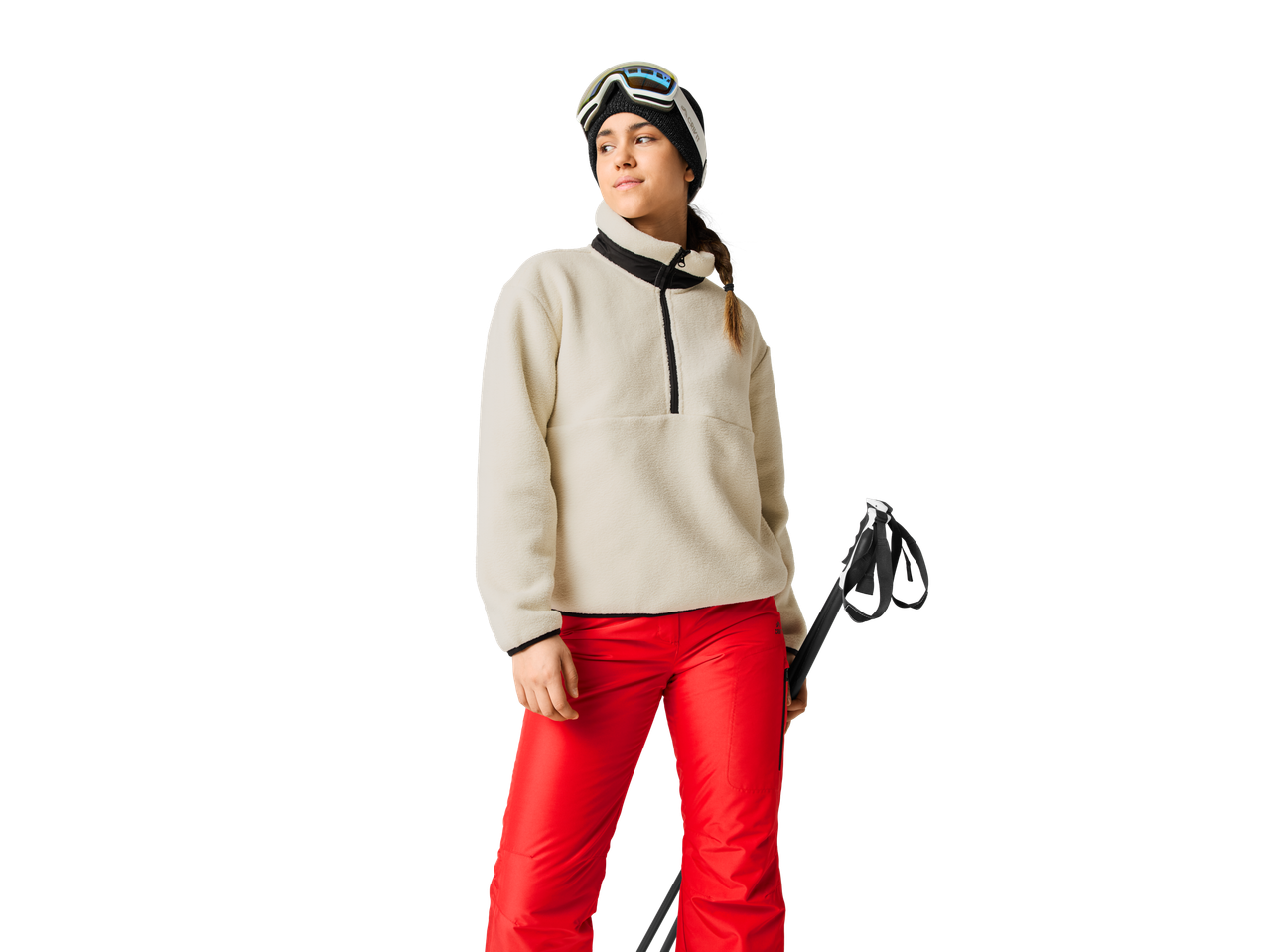 Woman in beige fleece, red ski pants, and ski goggles, holding ski poles.