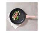 Frying pan with pink handle, containing cooked meat and vegetables on a white cloth.