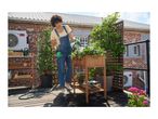 Woman watering plants in a raised wooden planter on a balcony garden.