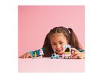 A girl playing with a LEGO Friends ice cream scooter and cart set on a pink table.