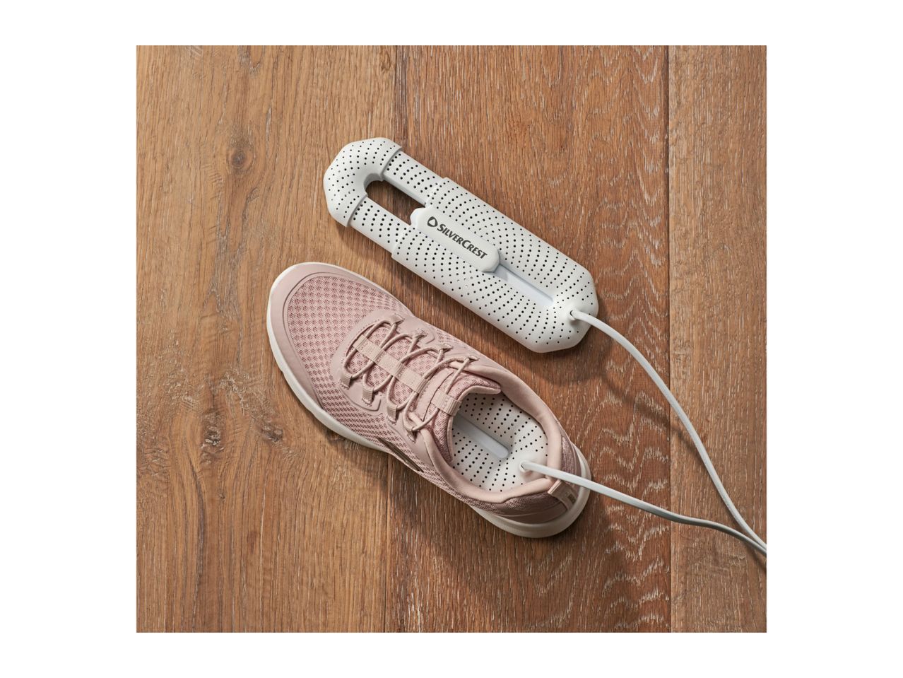 Electric shoe dryer next to a pink sneaker on a wooden floor.