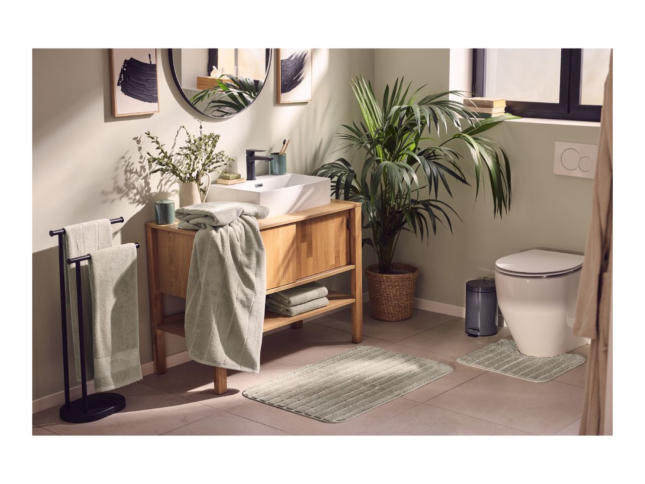 Bathroom with wooden vanity, white sink, black faucet, green towels, and plants.