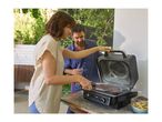 A couple grilling meat on an outdoor electric grill, with fries and wood pellets nearby.