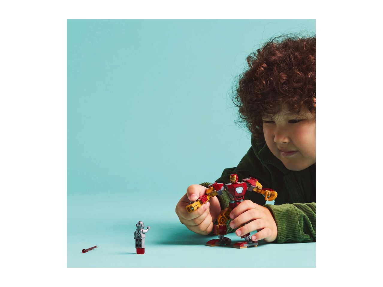 A child playing with a red and gold robot toy and a small silver robot figure.