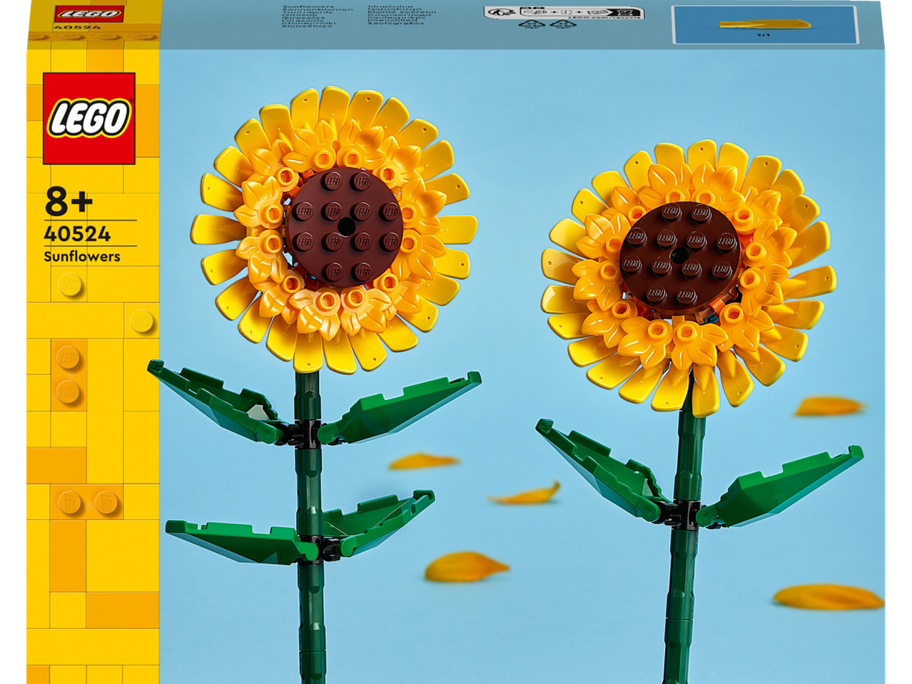 Divas dzeltenas rotaļlietu saulespuķes ar zaļiem kātiem un lapām, uz gaiši zila fona.