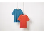 Δύο βαμβακερά t-shirt, ένα μπλε και ένα πορτοκαλί, κρέμονται σε έναν λευκό τοίχο.