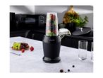 Black blender with fruit in a kitchen setting, with a bowl of fruit and glasses nearby.