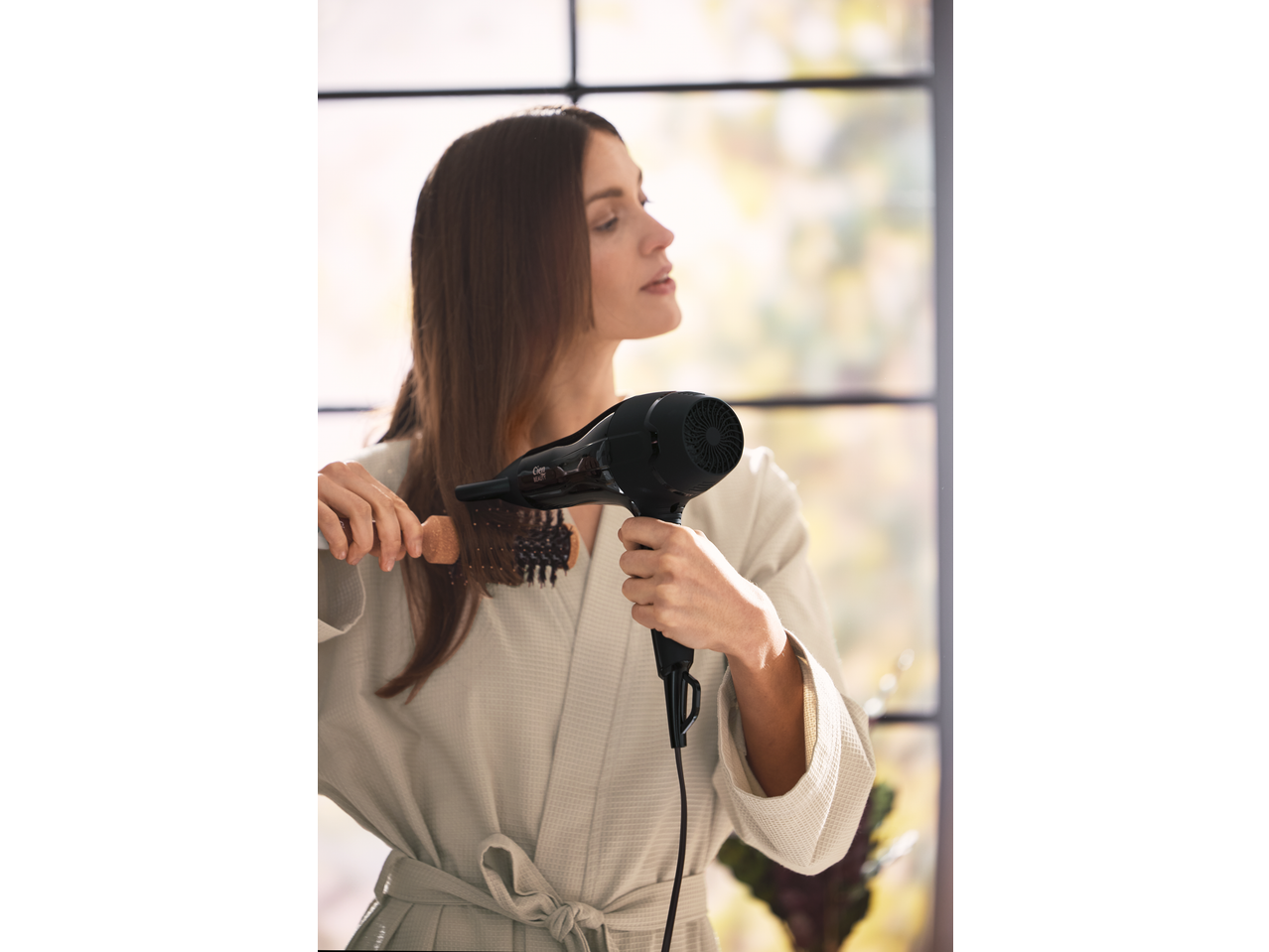 Femeie își usucă părul cu un uscător de păr Cien Beauty și o perie.